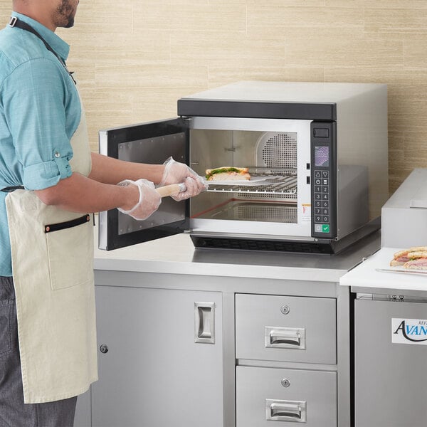 A man in an apron using an ACP XpressChef Jetwave countertop oven to cook food.