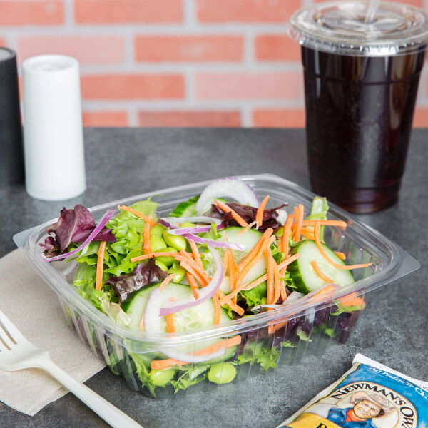 A Dart ClearPac rectangular plastic container filled with salad next to a drink.