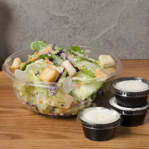 A salad in a Dart clear plastic bowl with three small cups of sauce.