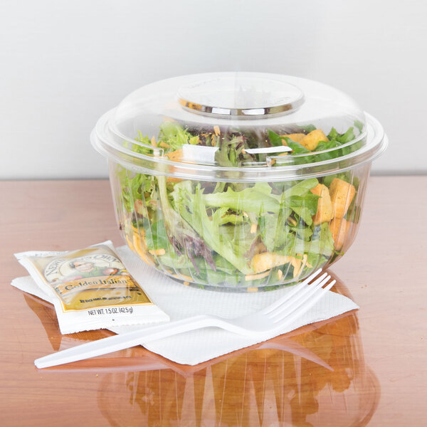 A clear Dart plastic bowl filled with salad and a white plastic fork.