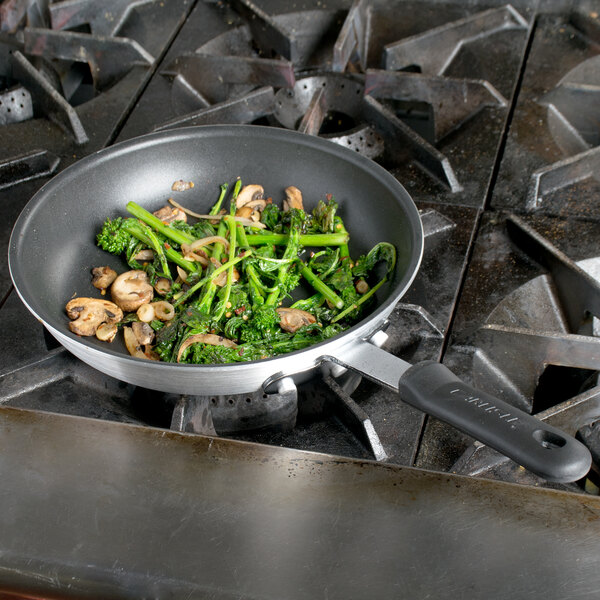 A Carlisle 10" aluminum non-stick fry pan with broccoli and mushrooms cooking on a stove.