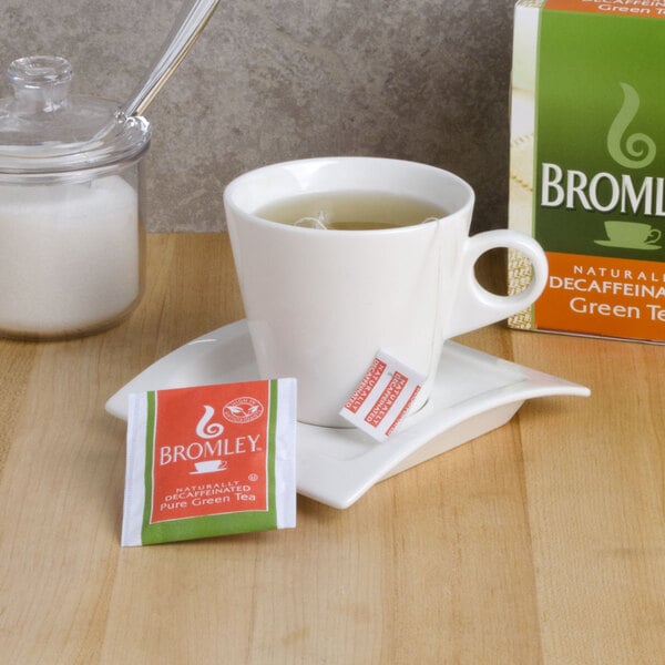 A cup of decaffeinated Bromley green tea with a tea bag on a saucer.