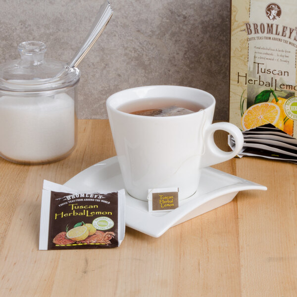 A cup of Bromley Exotic Tuscan Lemon Herbal Tea on a saucer with a packet of tea.