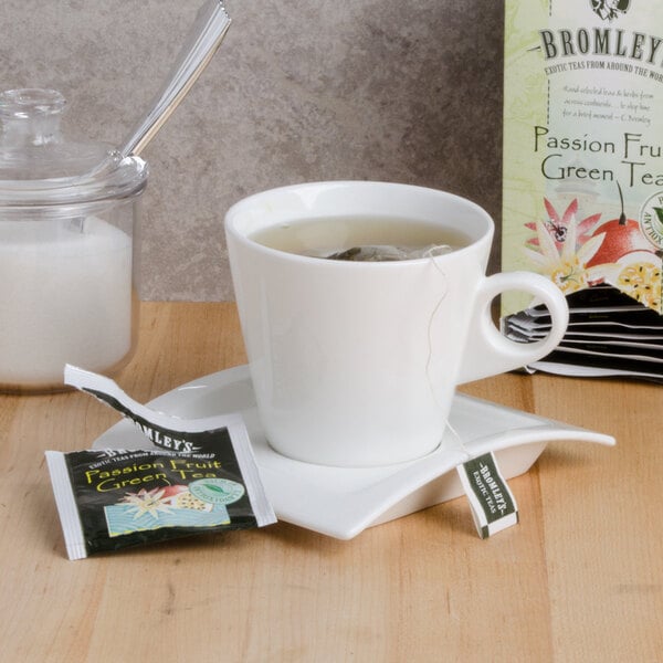 A cup of Bromley Exotic Passion Fruit Green Tea on a saucer next to a packet of tea.