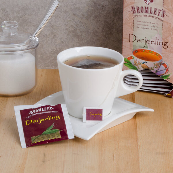 A cup of Bromley Exotic Darjeeling Tea with a tea bag in it on a table next to a box of Bromley Exotic Darjeeling Tea.