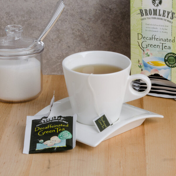 A cup of Bromley Exotic Green decaffeinated tea on a saucer with a tea bag in it next to a box of Bromley tea.