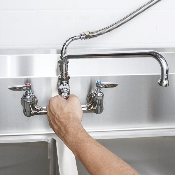 A person holding a T&S wall mounted pre-rinse faucet over a sink.