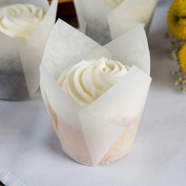 A Hoffmaster white tulip baking cup wrapped around a cupcake with white frosting.