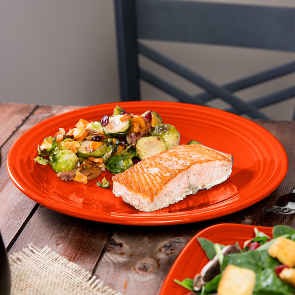 A Fiesta® round chop plate with a piece of salmon and vegetables on a table.