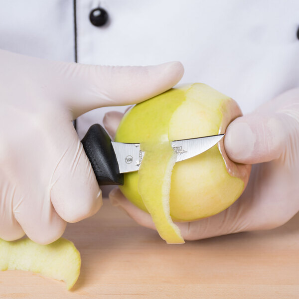 A person in a white coat using a Mercer Culinary Millennia peeling knife to peel a yellow apple.