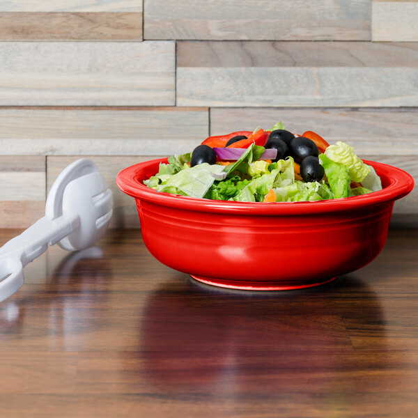A red Fiesta serving bowl filled with salad on a wooden table.