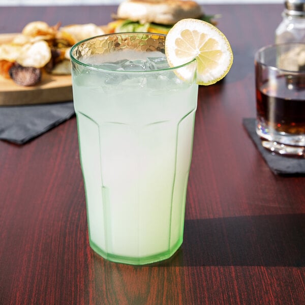 A close-up of a Cambro Spanish Green plastic tumbler filled with lemonade and ice with a lemon slice on the rim.