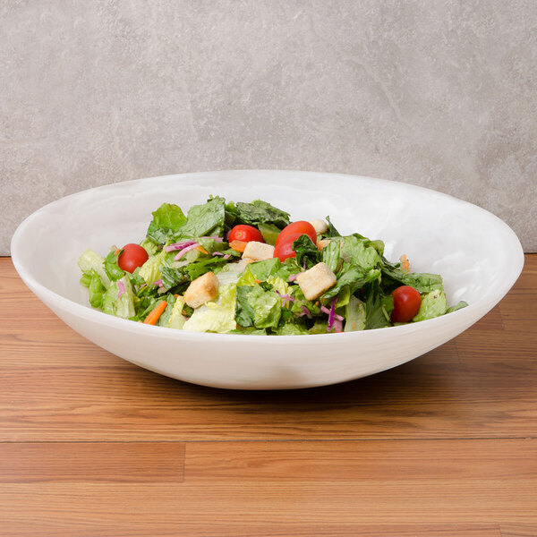 An American Metalcraft Translucence round bowl filled with salad on a wood table.