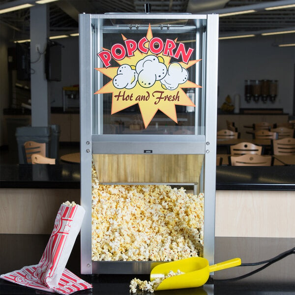 A Paragon popcorn warmer with a scoop and bags of popcorn on a counter.