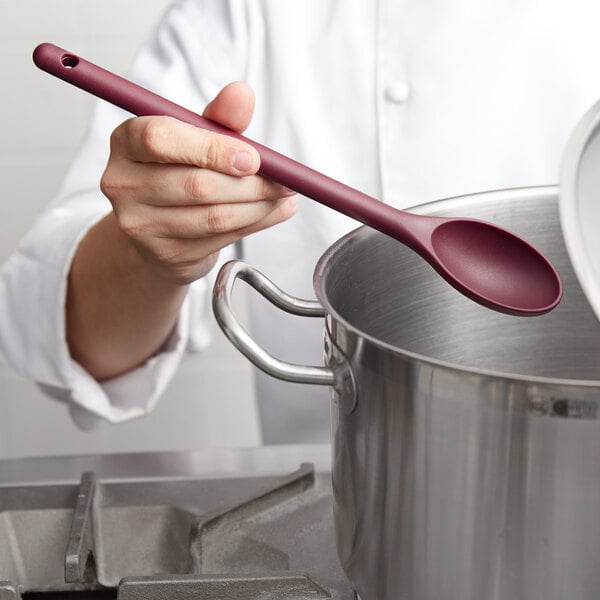A person holding a red Vollrath high heat nylon spoon over a pot.