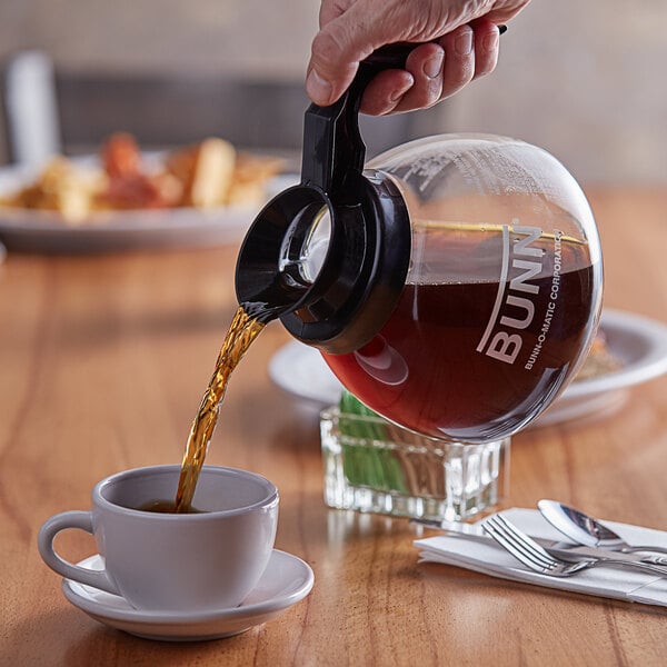 A person pouring coffee from a Bunn coffee pot into a cup.