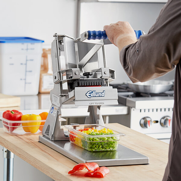 A person using an Edlund Titan Max-Cut Manual Dicer to cut yellow bell peppers.