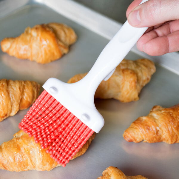 A hand using a Carlisle Sparta silicone pastry brush to baste croissants.