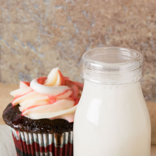A cupcake and a bottle of milk with an American Metalcraft round PET milk bottle cover on the table.