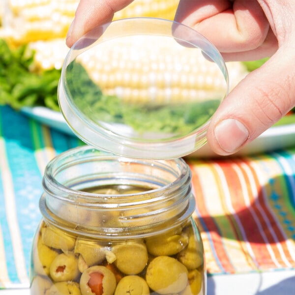 A hand holding an American Metalcraft PET round mason jar lid over a jar of olives.