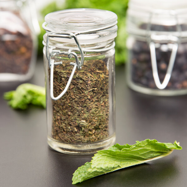 An American Metalcraft glass miniature apothecary jar filled with dried herbs.