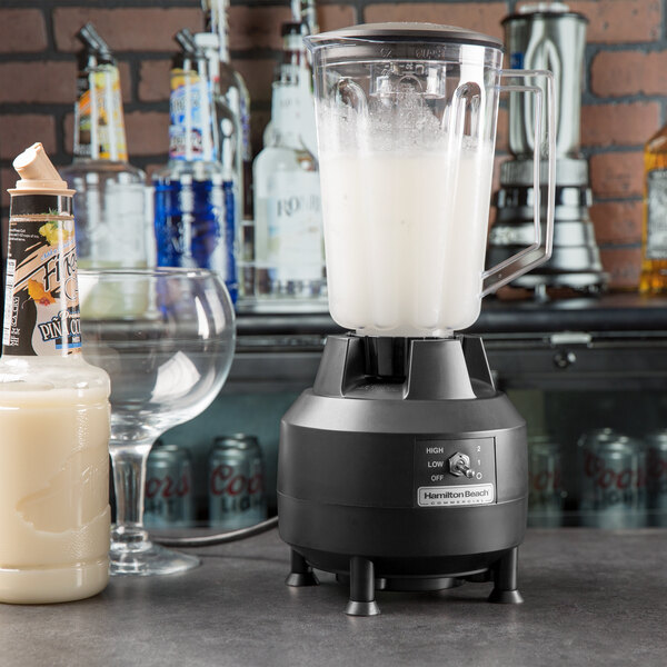 A Hamilton Beach commercial bar blender with a glass and a bottle of liquid on a counter.