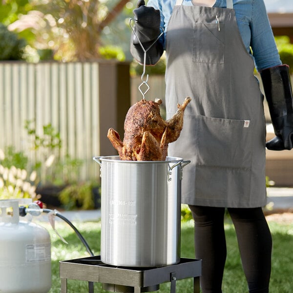 A woman cooking a chicken in a Backyard Pro aluminum pot over a gas flame.