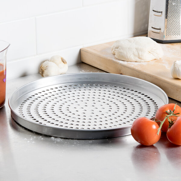 An American Metalcraft Super Perforated Aluminum Pizza Pan with tomatoes on it.
