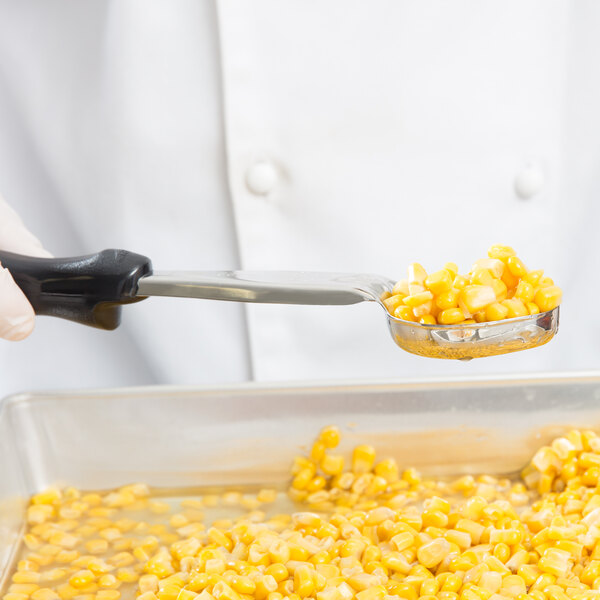 A person in a white coat using a Vollrath black perforated oval spoodle to serve corn.