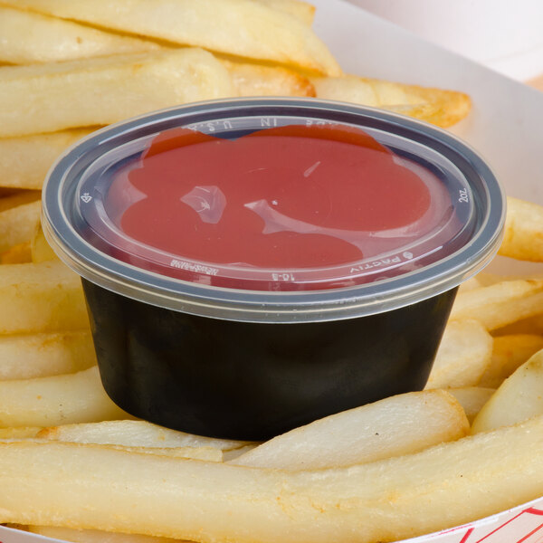 A clear oval plastic souffle lid on a container of ketchup on french fries.