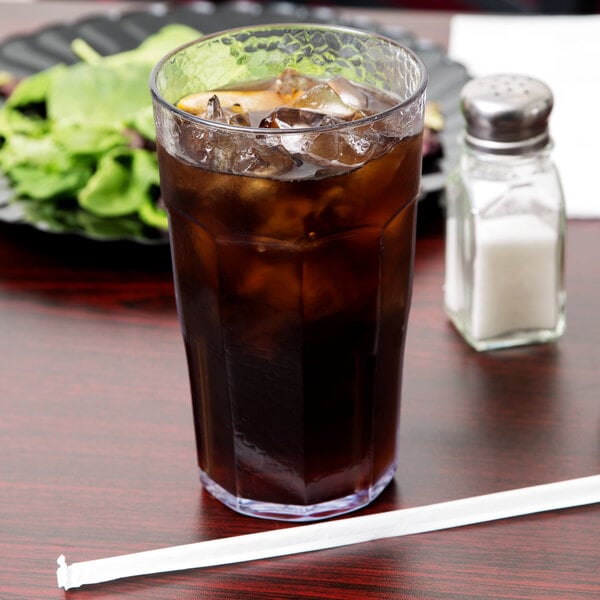 A Cambro Laguna clear plastic tumbler filled with ice tea on a table with a salad and salt shaker.
