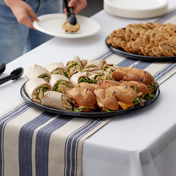 A Visions black plastic catering tray with sandwiches and cookies on a table.