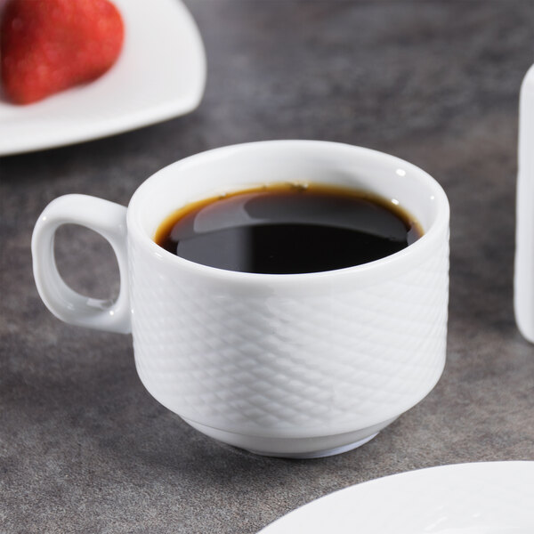 A CAC Super Bright White porcelain cup filled with coffee on a white saucer on a table.