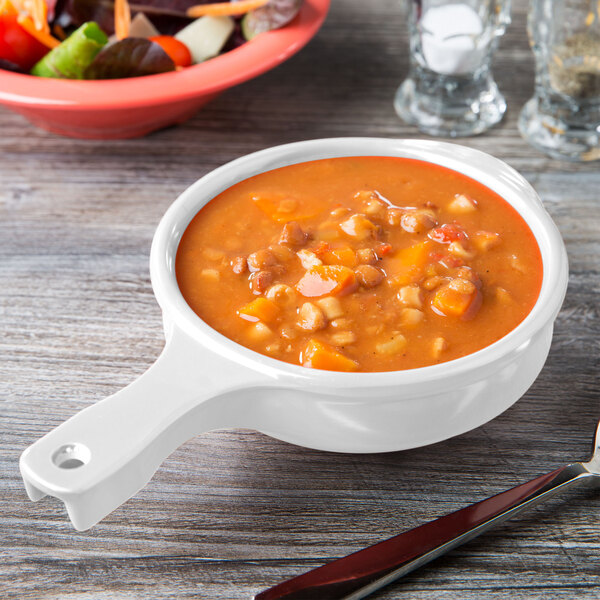 A Diamond White melamine bowl with a handle filled with soup on a table.