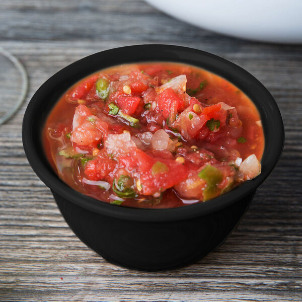 A black Elegance melamine bowl of salsa on a wood surface with a spoon next to it.