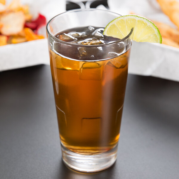 A Libbey stackable beverage glass of iced tea with ice and a lime wedge.