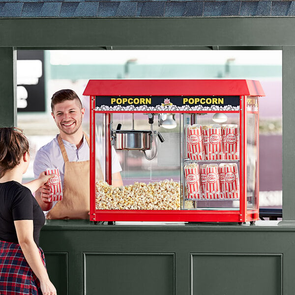 A man and woman standing in front of a Carnival King popcorn machine on a table.