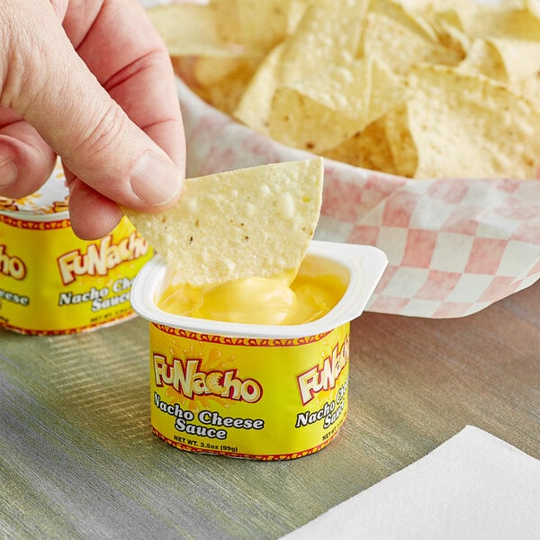 A person holding a chip and dipping it into a yellow container of FUNacho cheese sauce.