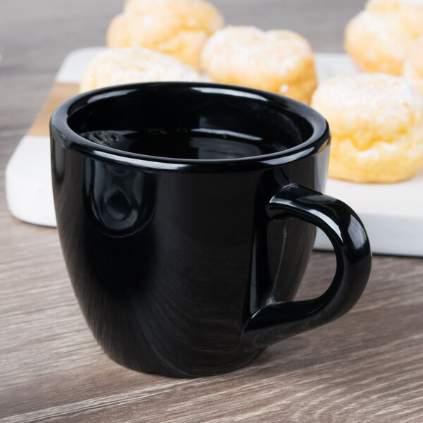 A black Elegance espresso cup with a few pastries on a wood surface.