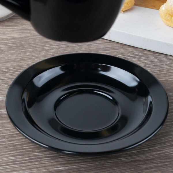 A black cup and saucer on a wood surface.