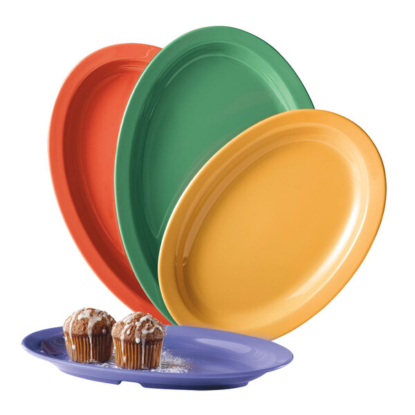 A stack of assorted Mardi Gras colored oval platters, including green and orange plates, with a muffin on one plate.