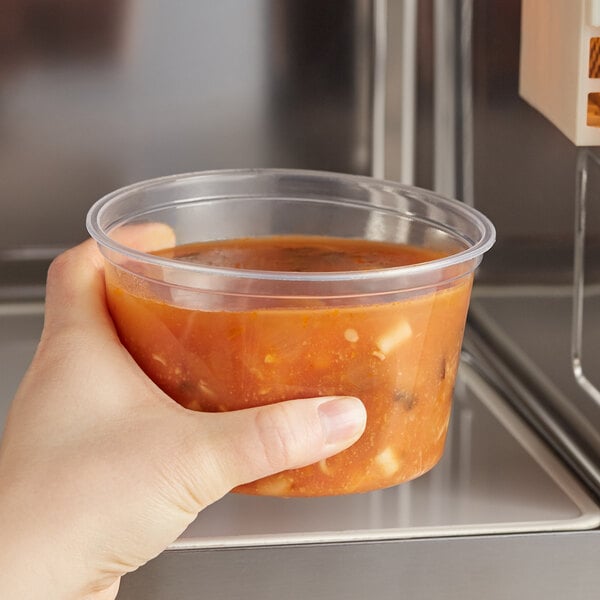 A hand holding a Choice translucent round deli container of soup.