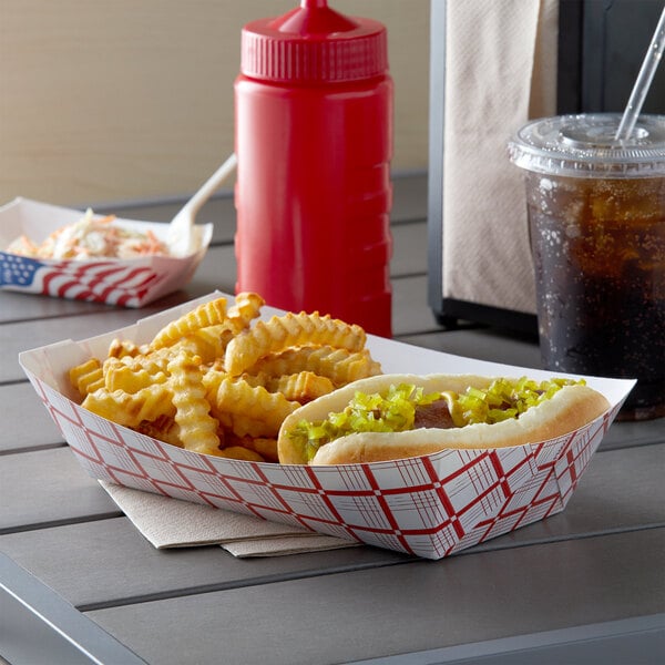 A hot dog and fries in a red check paper food tray on a table.