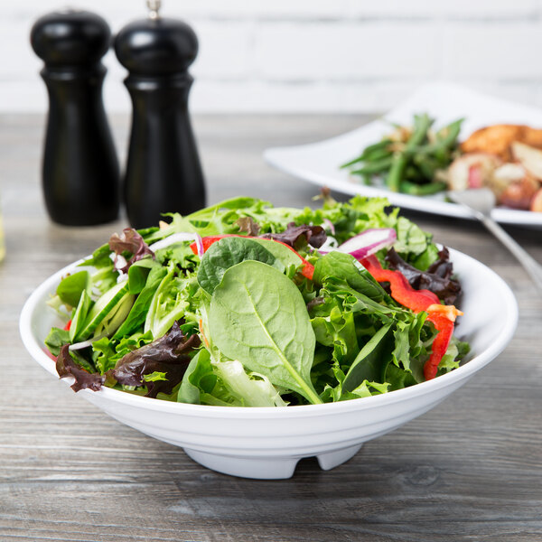A Milano white melamine bowl filled with salad on a wood table.