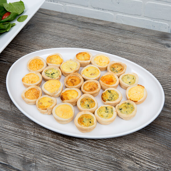 A white oval melamine platter with mini quiche on it.