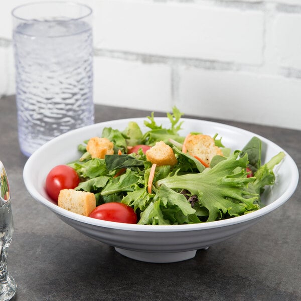A Milano white melamine bowl filled with salad next to a glass of water.