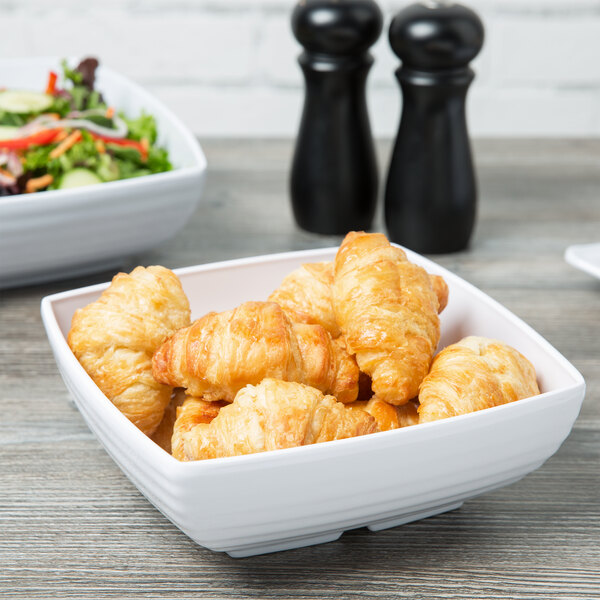 A white Milano square bowl filled with croissants and salad.
