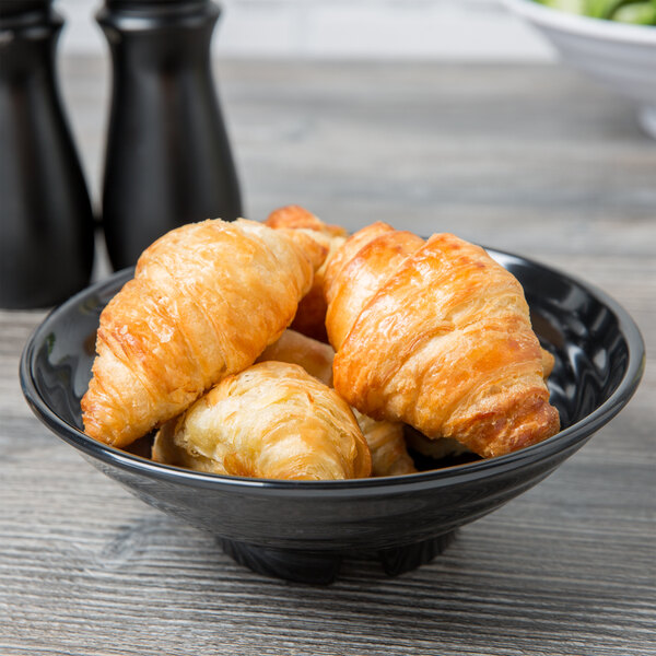 A black GET Milano melamine bowl filled with croissants on a table.