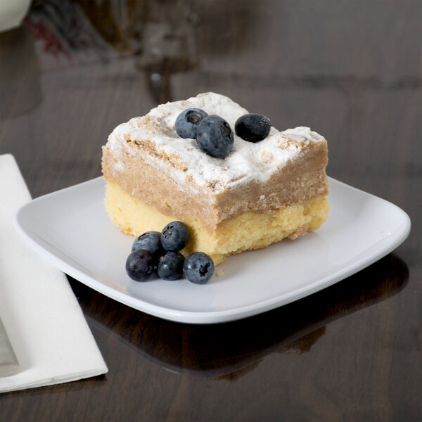 A piece of cake with blueberries on a white square coupe plate.
