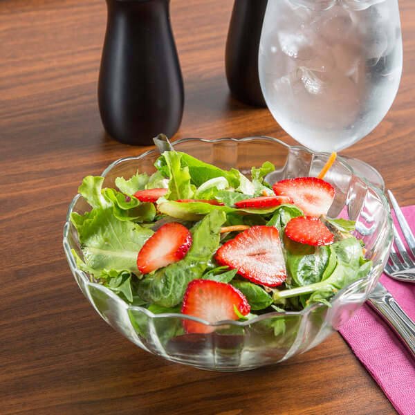 A bowl of salad with strawberries and greens in an Arcoroc glass bowl on a table with a glass of water.